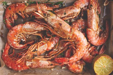 Sulu ızgara karides, parşömen kağıdıyla kaplanmış, otlar ve limonla süslenmiş fırın tepsisi..