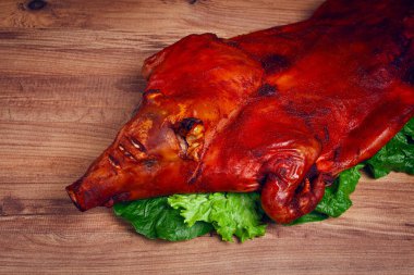 Pişmiş, kızarmış domuz yavrusu, ahşap bir masanın üzerinde, insan yok, bütün domuz yavrusu taze yeşil bir salatanın yapraklarıyla pişirilip sunuluyor, çıtır çıtır derisi ve detaylı özellikleri gösteriliyor..