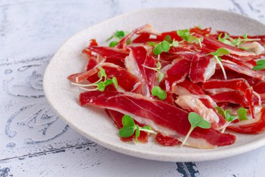Ham of duck breast,dried duck fillet, with microgreens,plate, on a tiled table,