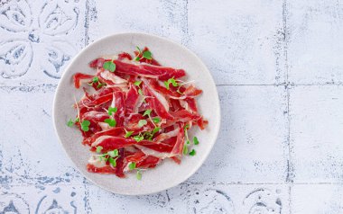Ham of duck breast,dried duck fillet, with microgreens,plate, on a tiled table,