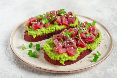 Taze ton balığı ve avokado ile kızarmış ekmek, siyah ekmek üzerine serpilmiş ve mikroyeşillikler serpiştirilmiş, kahvaltı, sağlıklı yiyecekler.