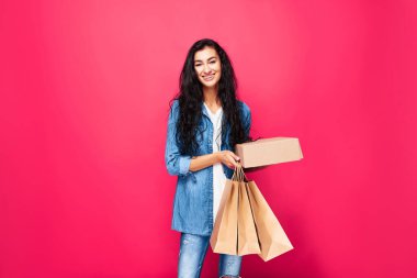 Alışveriş torbaları ve kutusuyla stüdyoda duran mutlu bir Arap kadın. Küçük kadınların eğlencesinin tadını çıkarıyorum. Pembe arka planda izole edilmiş günlük elbiseli bir kız. Alışveriş konsepti. Kurye.