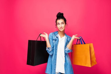 Stüdyoda alışveriş torbalarıyla bekleyen mutlu bir Arap kadın. Küçük kadınların eğlencesinin tadını çıkarıyorum. Pembe arka planda izole edilmiş günlük elbiseli bir kız. Alışveriş konsepti.