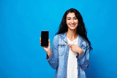Elinde akıllı telefonları olan çekici bir Arap kadın. Mavi arka plandaki stüdyoda izole edilmiş..