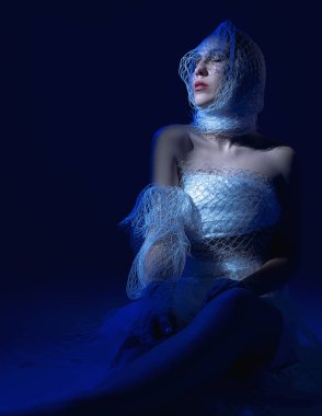 Beyaz elbiseli bir kız oturuyor ve mavi bir ışık parlıyor.