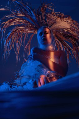 Palmiye yapraklı kadın oturuyor, mavi ve sarı ışık parlıyor.