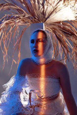 Palmiye yapraklı kadın oturuyor, mavi ve sarı ışık parlıyor.