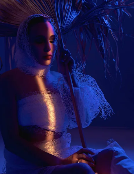 stock image woman with palm leaves sitting, blue and yellow light shining