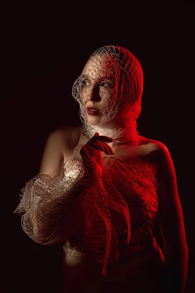 a girl wrapped in a net in the red light hides her face in the s