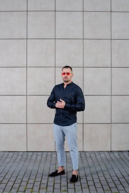 Arka planda siyah gömlekli, açık renk pantolonlu şık bir adam.