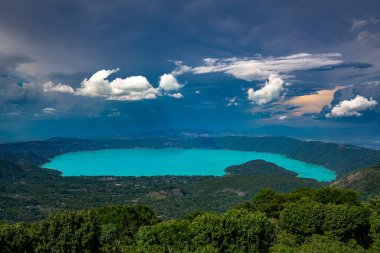 El Salvador 'daki Coatepeque Gölü' nün havadan görünüşü, mevsiminde suları fırtınalı bulutlarla dolu gökyüzü ile turkuaz rengine bürünür.