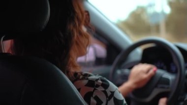 Kadın sürücü ustalıkla araba kullanıyor. Yoğun yolda araba kullanmadaki uzmanlığını gösteriyor. Kıvırcık saçlı beyaz kadın araba sürmeyi öğreniyor.