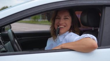 Mutlu araba sahibi dişlerinde anahtar tutuyor. Neşeli genç bir kadın yeni otomobil salonunda oturuyor ve anahtarlarını ağzında gösteriyor, deli gibi görünüyor. Araba satın al ya da kirala