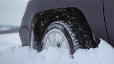 Karlı kırsal yolda araba sürerken arabaların tekerlekleri patinaj yapıyor. Kış yolunda yol tutuşu kazanmaya çalışan SUV aracı karlı parçalar kusuyor.