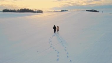 Karda el ele tutuşan romantik yetişkin bir çift, güzel güneş ışığıyla geçen aşk zamanı, kırsal kesimde, yel değirmeni türbinlerinin yanında günbatımında alevler, hava manzarası. Yolculuk ve sağlıklı aktif
