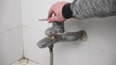 Banyodaki kırık musluk, tanınmayan bir adam su akışı için musluğu açtı. Duvar kiremitlerinde küf olan eski banyoda tesisat tamiri.