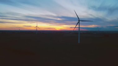 Hava görüşlü rüzgar türbini rüzgar gücüyle dönüyor ve yeşil ekolojik yolla yenilenebilir enerji üretiyor. Akşamları büyüleyici renkli bulutlu güneş batışı. Rüzgar tarlası yeşil enerji üretiyor.