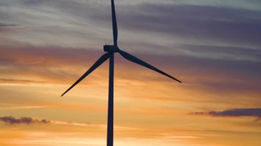 Geniş rüzgar türbini, saha manzaralı bıçaklar, rüzgâr değirmenleri, dramatik bulutlu pembe turuncu günbatımında siluet. Siluetler yel değirmenleri, büyük turuncu güneş diski yaz merceği parlamaları. Alternatif enerji