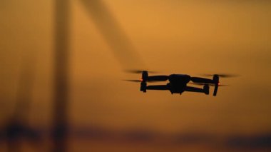 Drone rüzgar türbinlerinin çiftliğini inceliyor. Soluk kesen bulutlu günbatımında. Kuadrokopter, elektrik istasyonunun avantajlarını ve dezavantajlarını araştırıyor. Ekoloji Güvenli Alternatif Enerji Kaynağı