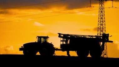 Tanımlanamayan siluet erkek çiftçi gecenin karanlığında büyüleyici renkli bulutlu güneş batımında tarlaları ilaçladıktan sonra güçlü bir traktörle çalışıyor. Tarım sektöründe modern, güçlü tarım yöntemlerini kullanarak çalışmak