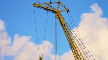 Mavi gökyüzünde hareket eden bulutlarla dolu bir depoda büyük bir elektrikli vinç. Kargo yüklemesi için sarı vinç