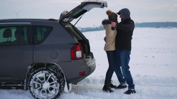 スノーフィールドのオープンカーのトランクの近くで男と女を抱きしめる笑顔のダンス 寒い冬の季節に自然に関する家族の夫と妻の活動 旅と健康的なアクティブライフスタイルのコンセプト — ストック動画