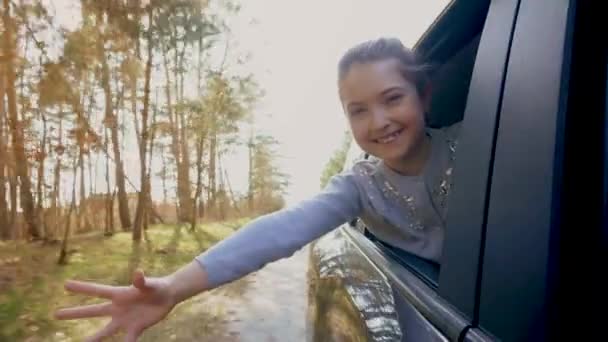 Весела Маленька Дівчинка Дивиться Крізь Вікно Відкритого Автомобіля Викладаючи Руку — стокове відео