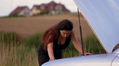 Endişeli kadın arabanın kaputunun önünde durmuş aşırı ısınmış motora bakıyor. Kadın Sürücü Hasar Aracı 'nı inceliyor. Yol kenarında Otomobil Sorunu