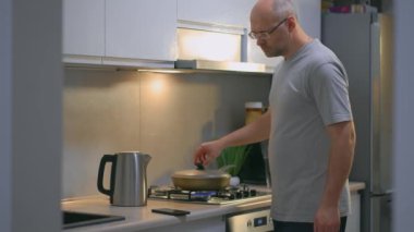 Adam mutfakta tavada kızarmış tavuk eti pişirirken cep telefonundan video tarifi izliyor. Hobi, yemek hazırlama, modern iç mekan, aşçılık konsepti.