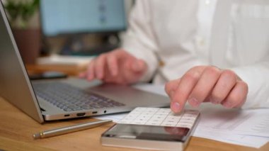 Ofiste çalışan adam, dizüstü bilgisayar ve hesap makinesi kullanan masa başına yerleştirilen adam vergileri sayıyor. Erkek Freelancer evden çalışıyor. İnternet taranıyor, sosyal ağlar kullanılıyor