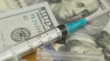Şırınga paranın üzerinde dönüyor, kapat. Sağlık sigortası konsepti. Dolar banknotlarının arka planında şırınga var. Ağır çekim, yakın çekim.