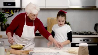 Pişirme. Büyükanne ve öğrenen kız mutfakta turta ve çörek pişiriyor. Öğretmenlik. Çocuk hamur parçalarını doldurmaya yardım ediyor. Mutlu büyükanne ve torun evde yemek pişiriyor.