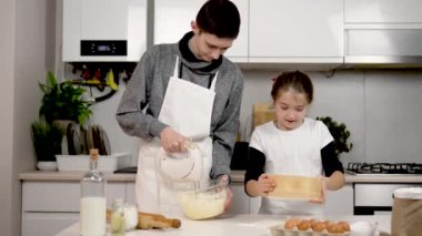 Çocuk cam kasede krema çırpıyor ve mutfakta mikser var. Kremalı tatlı. Küçük kız asistan kardeşime yardım ediyor ve beyaz unu süzgeçten geçiriyorlar. Masaya hamur diz. Ergen çocuklar yemek yapıyor.