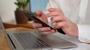 İşadamı, bilgisayar ve hesap tablosu veya iş stratejisi üzerinden şirketlerin kârını analiz ederken, iş arkadaşlarıyla iletişim kurmak ve kontrol etmek için akıllı telefon kullanır. Bilgisayar kullanan profesyonel bir erkek.