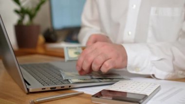 Adam bir tomar doları yakın tutuyor, iş adamı nakit paraları sayıyor ve hesap makinesinden maddi kazancı hesaplıyor. Modern bilgisayar kullanan profesyonel bir erkek ofis masasında oturuyor.