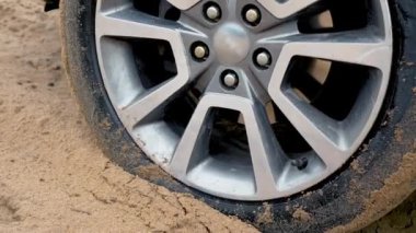 Kirli kır yolunda ıslak kuma sıkışmış dönen bir araba çarkı. Döner lastikler kapanıyor. Çölde, kumda, off-road 'da yol tutuşu kazanmaya çalışan SUV aracı.
