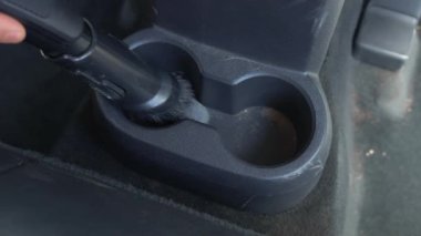 Kirli arabanın içini temizlemek için elektrikli süpürge kullanan erkek elleri. Bardak tutucuları yakın çekim. Araba servisi çalışanı elektrikli süpürge kullanıyor.