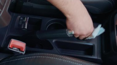 Araba bakımı. Tamirci, konsol tutacağı temizlemek için nemli bez ve toz ve kirden el freni kullanır. Adam arabanın içini nemli bez ve deterjanla yıkıyor.