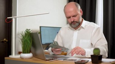 Adam Ofiste Dizüstü bilgisayarla oturuyor, Para Yığını Konsantre Oluyor. Olgun, orta yaşlı, orta yaşlı, ofis masasında çalışan yetişkin bir adam.
