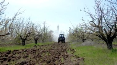 Tarlada terk edilmiş meyve bahçesinde çalışan böcek ilacı püskürtücü traktörü. Bahçecilik, bahçıvanlık. Bahçıvan traktör bahçesi sürüyor ve mahsul koruma ürünleri püskürtüyor