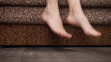 Sabahın erken saatlerinde kadınlar çıplak ayakla yatmayı severler. Kadın bacakları kanepeden kalkıyor. Dişi bacaklar aşağı iniyor. Ayak parmakları parke ya da lamine.