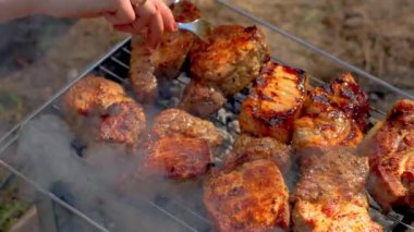 Tanınmayan bir kadın sıcak odun kömürü tüttürürken nefis kokulu et pişiriyor. Sıcak, sulu ızgara et parçaları. Izgara çizgili sulu biftek piknik kutlaması için hazırlanıyor.
