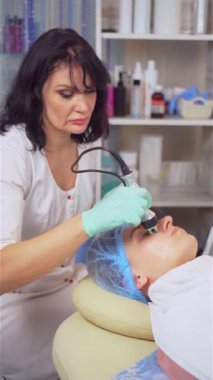 Dikey çekim. Güzellik içinde yükselmek. Estetik kozmetolojinin merkezinde gençleştirme ve yaşlanma karşıtı yüz derisi için bir cihaz. Güzellik uzmanı kadınlar için yüz yenileme prosedürü uyguluyor.