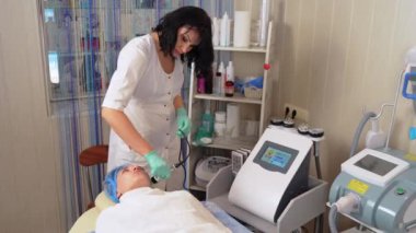 Profesyonel kadın kozmetik uzmanı güzellik salonunda yatan kadının yüz gerdirme ameliyatı için yüz ultrasonu yapıyor. Ultrasonik oyuk yüz şekillendirme prosedürü