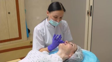 Cerrah, tıbbi eldivenlerle kadın dudaklarına hyaluronik asit enjekte ettikten sonra dikkatlice ve yavaşça masaj yapıyor. Dişi dudak büyütme. Kozmetik enjeksiyonlar, gençleştirme