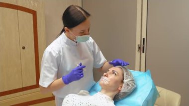 Güzellik uzmanı genç kadın yüzünde işaretler yapar. Kırışıklıklara karşı botulinyum tedavisi. Güzellik salonundaki kozmetoloji prosedürü, deneyimli uzman kadın yüzüne botulinyum enjekte ediyor.