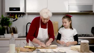 Yaşlı bir kadın hamur mayasını mutfak masasında beyaz un ile sarıyor. Şirin kıza yemek yapmayı öğret. Çocuk büyükanneye yardım ediyor. Aile aşçılığı bilgi ve deneyimi paylaşır. Bıçakla hamuru kes