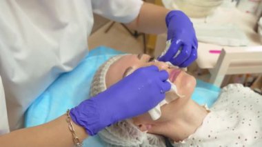 Spa salonunda kozmetik uzmanı kadın yüzünü pamuklu mendille temizliyor. Güzellik salonundaki kadın yüz bakımını alıyor. Yan görüş, yakın çekim.
