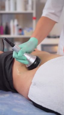 Ultrasound cavitation vücut hatları tedavisinin dikey videosu. Spa tedavisi. Kadın mide için anti-yağ tedavisi görüyor, yakın çekim. Ultrason boşluğu ve vücut bakımı