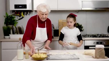 Büyükanne küçük kıza patatesli turta pişirmeyi öğretiyor. Ev işleri aile nesillerine yardım ediyor. Torunum hamur dolgulu çörek yapar.